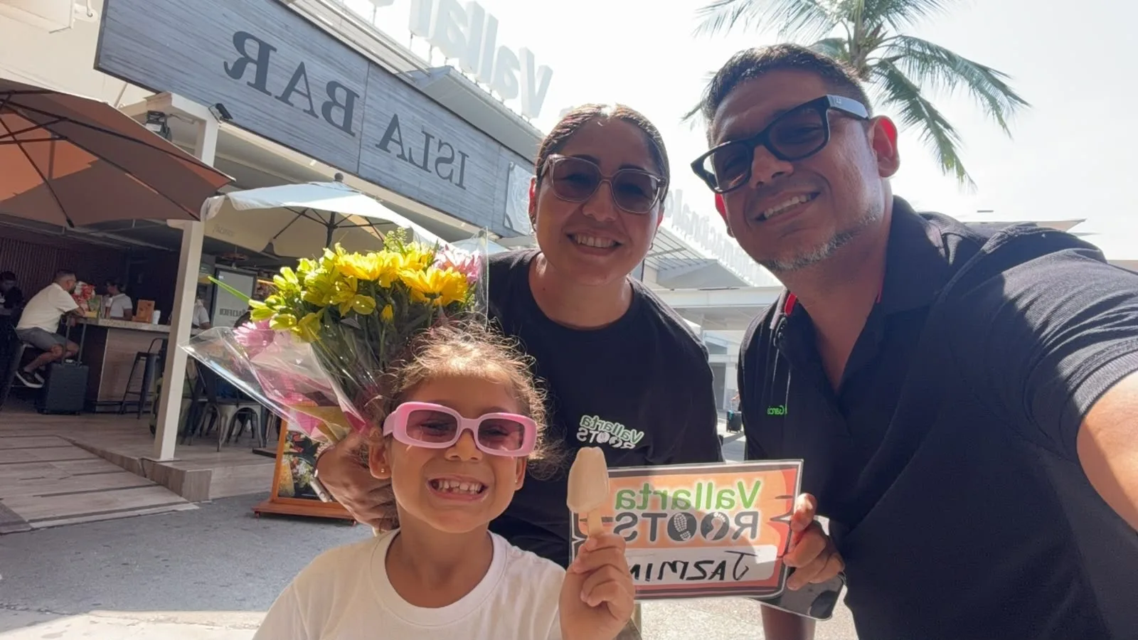 The García family welcoming a guest at Puerto Vallarta airport with flowers and a Vallarta Roots sign