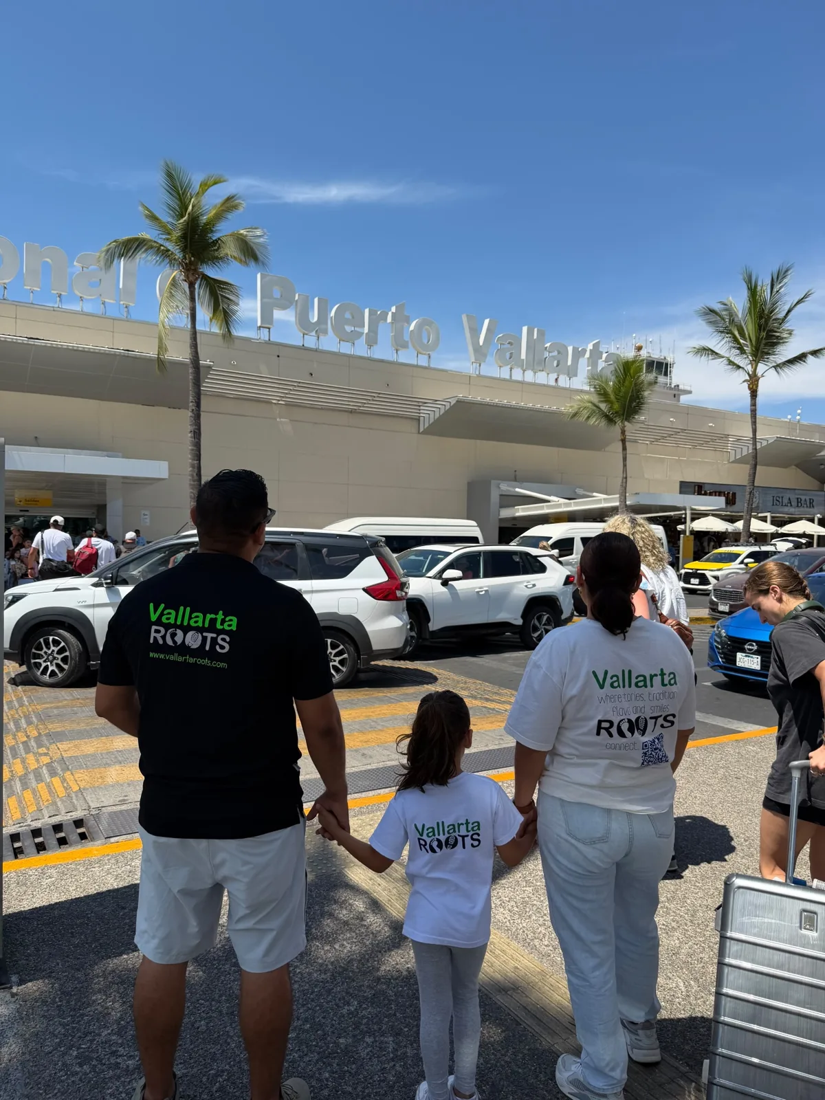 Pepe, his wife and daughter in Vallarta Roots shirts holding hands outside Puerto Vallarta International Airport