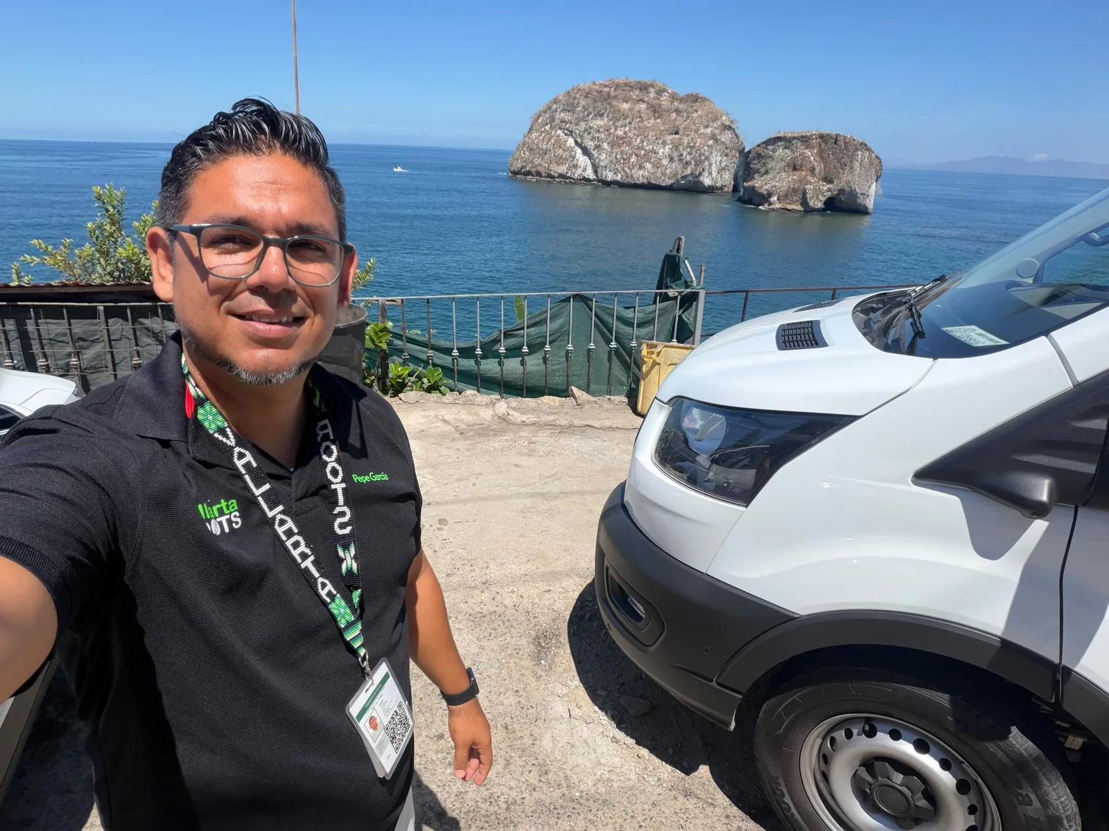 Pepe García beside a Vallarta Roots vehicle with Los Arcos on the coast behind him